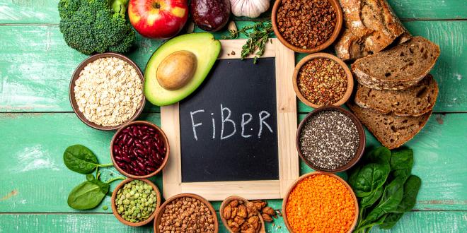 The word fiber on a blackboard slate surrounded by food sources of fiber, like avocado, beans, and lentils.