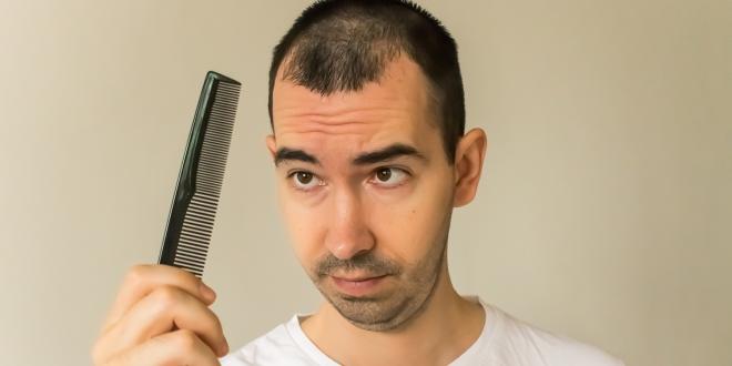 a middle-aged man looking at his comb with worry